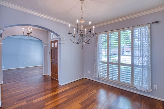 unfurnished dining area featuring arched walkways, ornate columns, a chandelier, wood finished floors, and ornamental molding