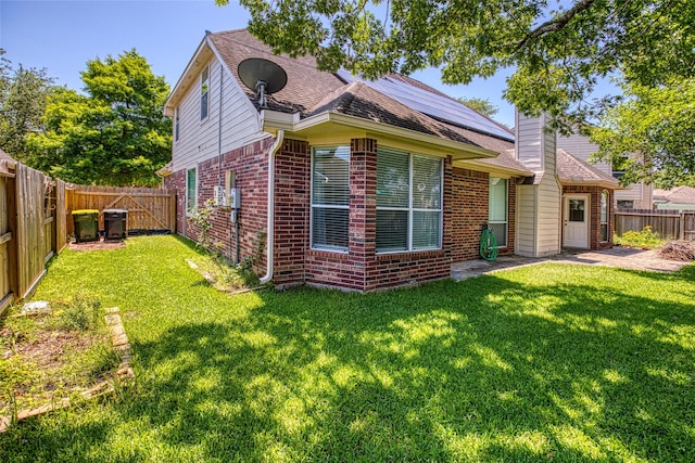 rear view of property featuring brick siding, solar panels, a chimney, and roof with shingles