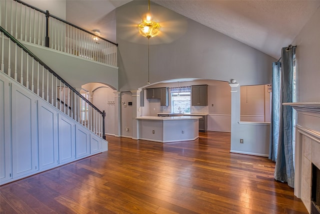 unfurnished living room with arched walkways, decorative columns, a ceiling fan, dark wood-type flooring, and high vaulted ceiling