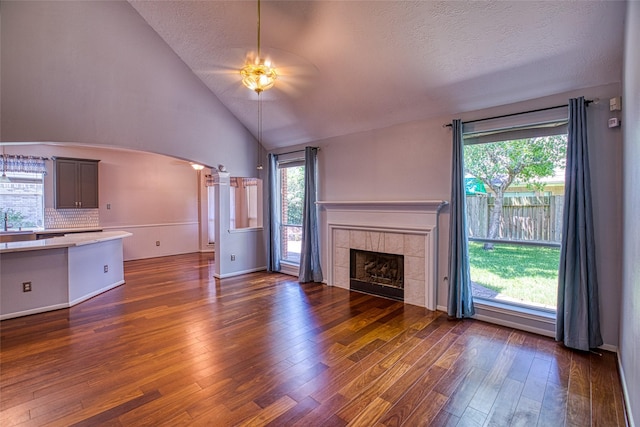 unfurnished living room featuring arched walkways, dark wood finished floors, ceiling fan, a fireplace, and vaulted ceiling