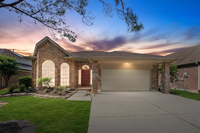 view of front of house with a shingled roof, an attached garage, brick siding, concrete driveway, and a yard