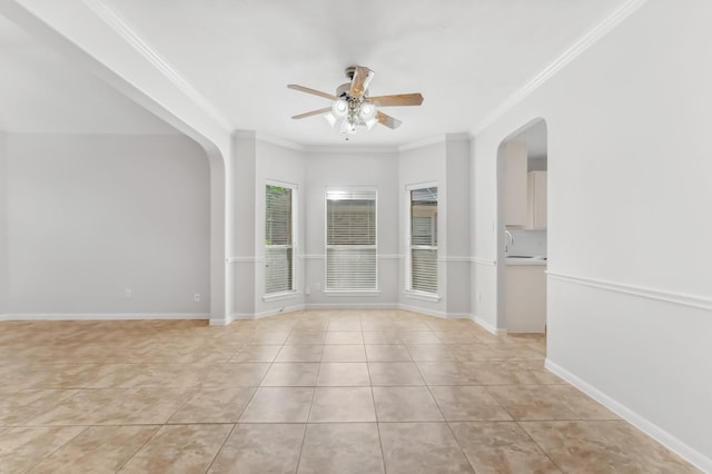 empty room featuring light tile patterned flooring, a sink, arched walkways, a ceiling fan, and ornamental molding