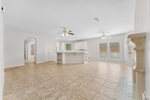 unfurnished living room featuring arched walkways, ceiling fan, light tile patterned flooring, and visible vents