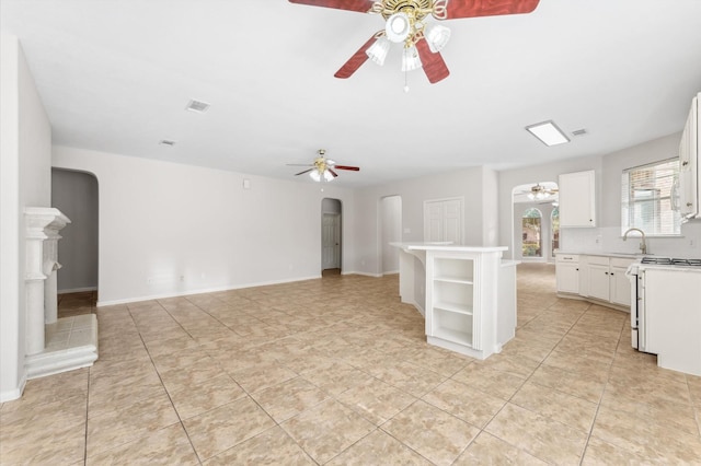unfurnished living room with arched walkways, ceiling fan, visible vents, and a sink