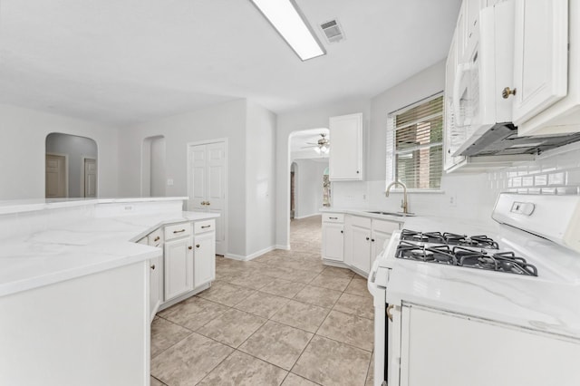 kitchen with white appliances, arched walkways, white cabinets, and a sink