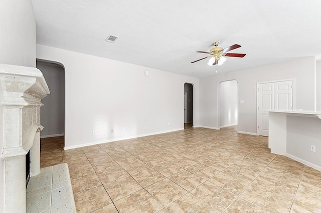 unfurnished living room featuring visible vents, baseboards, ceiling fan, arched walkways, and light tile patterned floors