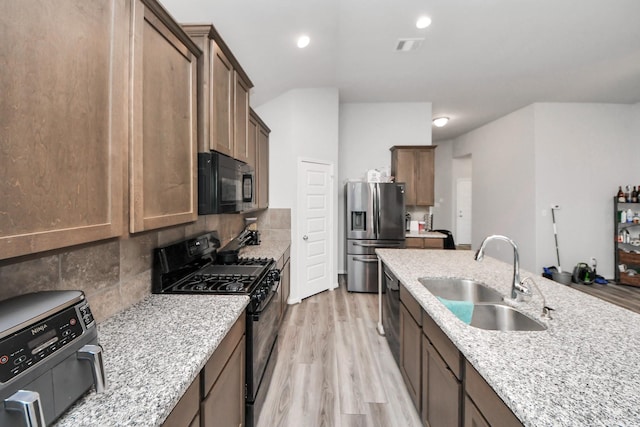 kitchen featuring light stone counters, a sink, light wood finished floors, backsplash, and black appliances