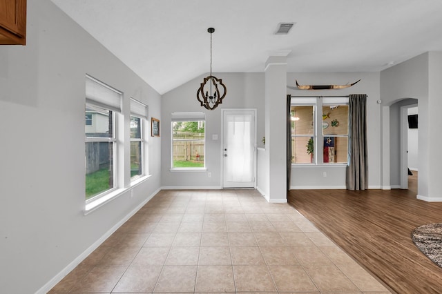entryway featuring arched walkways, a chandelier, light tile patterned floors, lofted ceiling, and visible vents