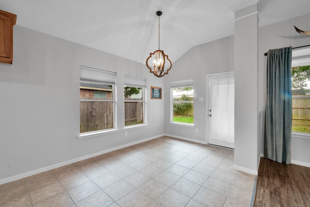 entryway with light tile patterned floors, plenty of natural light, vaulted ceiling, and an inviting chandelier