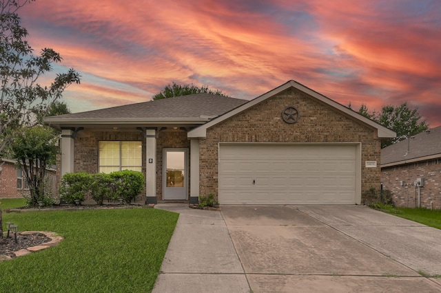 ranch-style house with roof with shingles, an attached garage, brick siding, a yard, and driveway