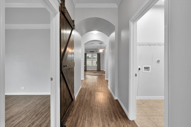 hallway featuring crown molding, arched walkways, a barn door, and wood finished floors