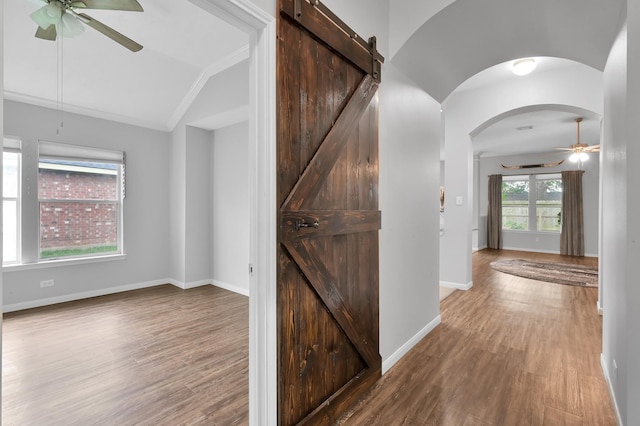 corridor with arched walkways, wood finished floors, vaulted ceiling, and a barn door