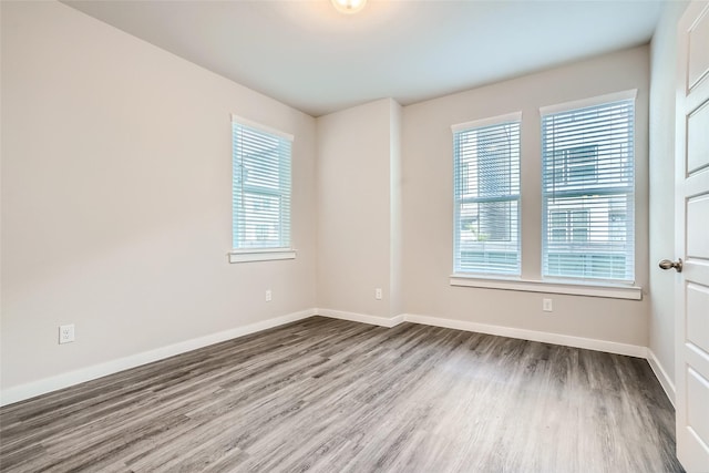 unfurnished room featuring baseboards, a wealth of natural light, and wood finished floors