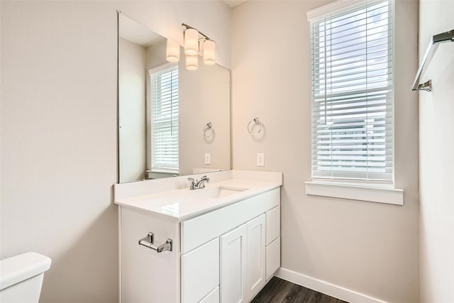 half bath featuring toilet, baseboards, wood finished floors, and vanity