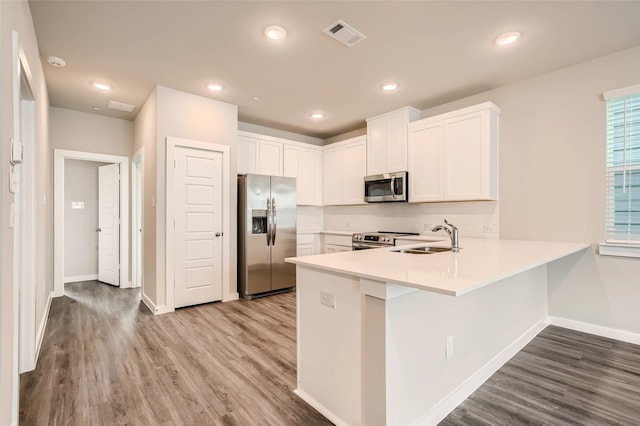 kitchen with a sink, appliances with stainless steel finishes, a peninsula, and wood finished floors