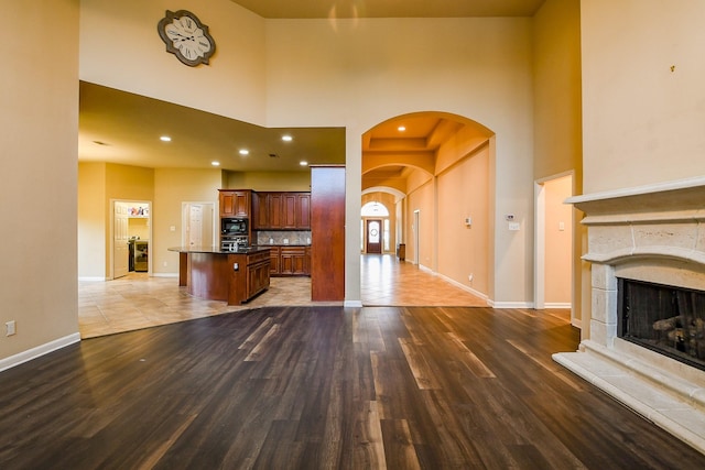 629 Pelican Harbour Dr, Texas City, TX 77590 - unfurnished living room featuring arched walkways, a towering ceiling, wood finished floors, baseboards, and a fireplace with raised hearth
