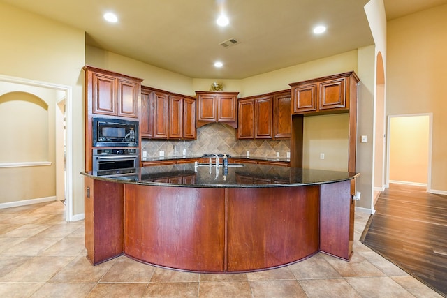 629 Pelican Harbour Dr, Texas City, TX 77590 - kitchen with stainless steel oven, black microwave, decorative backsplash, dark stone counters, and an island with sink