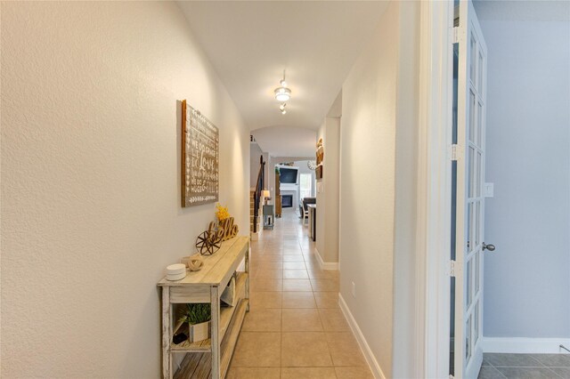 corridor with arched walkways, baseboards, and light tile patterned flooring