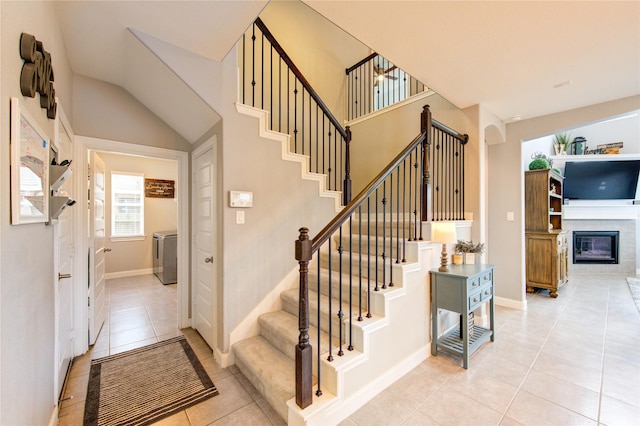 staircase featuring washer / dryer, tile patterned floors, baseboards, and a glass covered fireplace