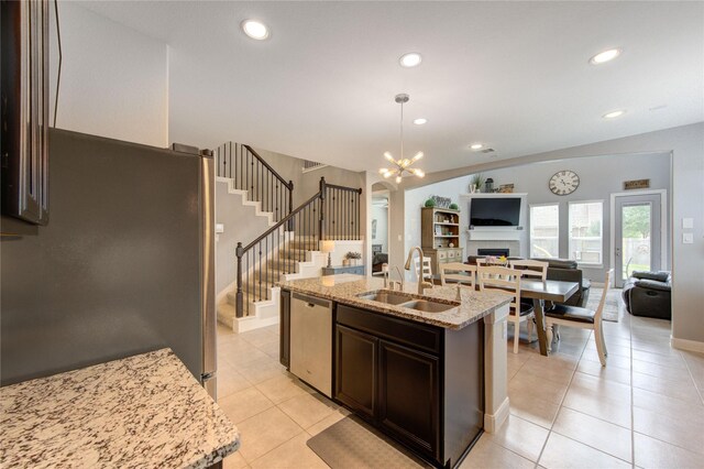 kitchen with dark brown cabinetry, a fireplace, open floor plan, a sink, and stainless steel appliances