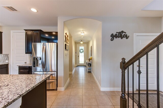 kitchen with dark brown cabinetry, visible vents, light stone countertops, stainless steel fridge with ice dispenser, and light tile patterned flooring