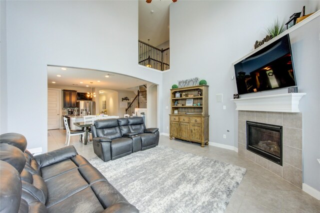 living room with a fireplace, a high ceiling, stairway, arched walkways, and light tile patterned floors