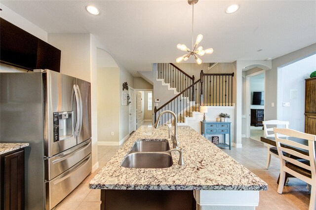 kitchen featuring arched walkways, a sink, stainless steel fridge with ice dispenser, light tile patterned floors, and an island with sink