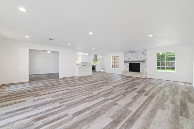 unfurnished living room with a stone fireplace, light wood-style flooring, recessed lighting, baseboards, and visible vents