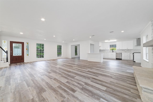 unfurnished living room featuring recessed lighting, light wood-style flooring, a wealth of natural light, and stairway