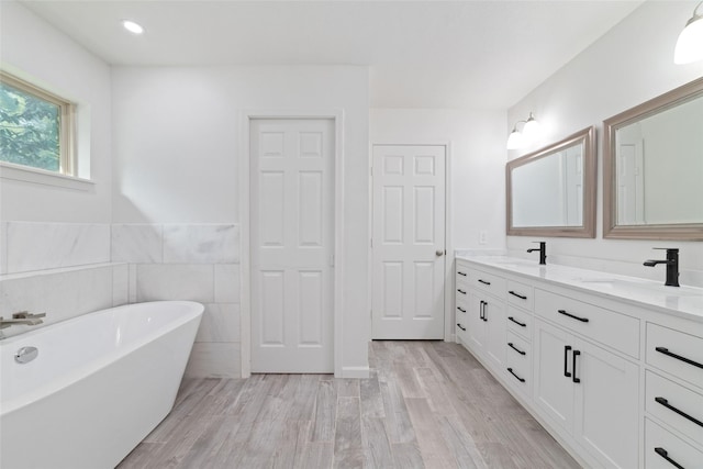 bathroom featuring double vanity, a soaking tub, a sink, and wood finished floors