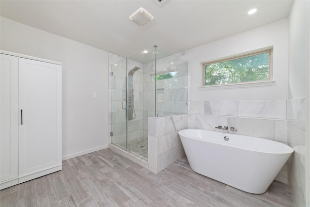 full bath featuring a freestanding tub, tile walls, a shower stall, and wood finished floors
