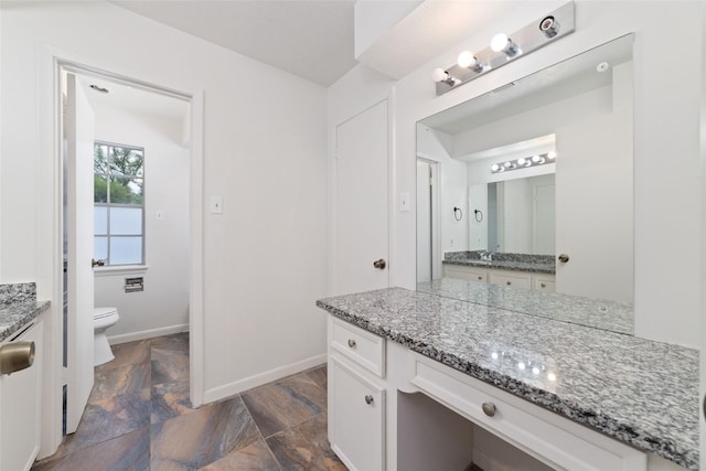 bathroom with vanity, stone finish flooring, baseboards, and toilet