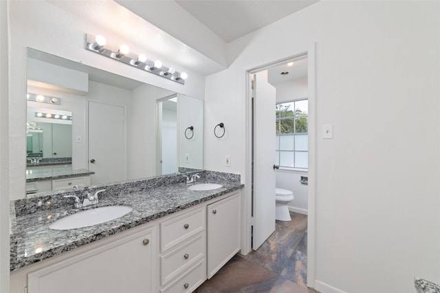 bathroom with double vanity, toilet, baseboards, and a sink