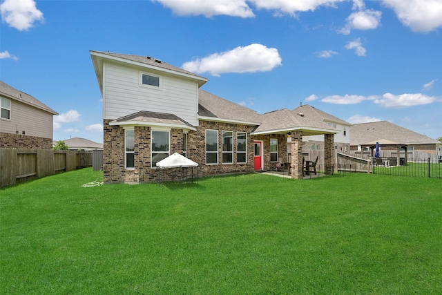 rear view of property featuring a shingled roof, brick siding, a fenced backyard, a lawn, and a patio