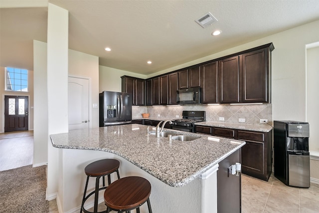 kitchen featuring dark brown cabinetry, visible vents, light stone countertops, a sink, and black appliances