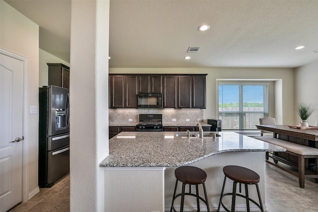 kitchen featuring visible vents, dark brown cabinetry, light stone counters, a sink, and black appliances