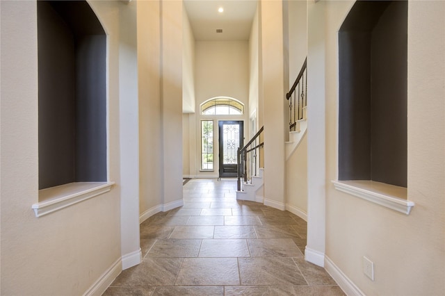 entrance foyer featuring baseboards, stairs, a towering ceiling, and stone tile floors