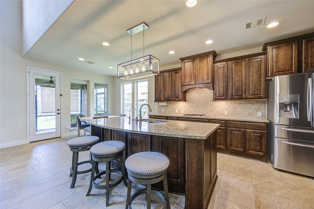 kitchen with appliances with stainless steel finishes, light stone counters, a breakfast bar area, tasteful backsplash, and visible vents