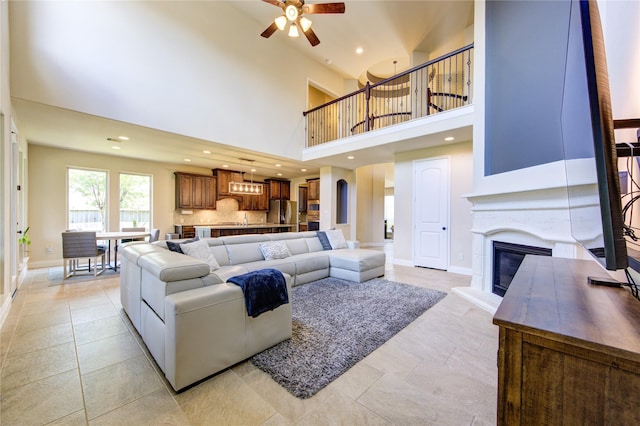 living room with a ceiling fan, a towering ceiling, baseboards, a glass covered fireplace, and recessed lighting