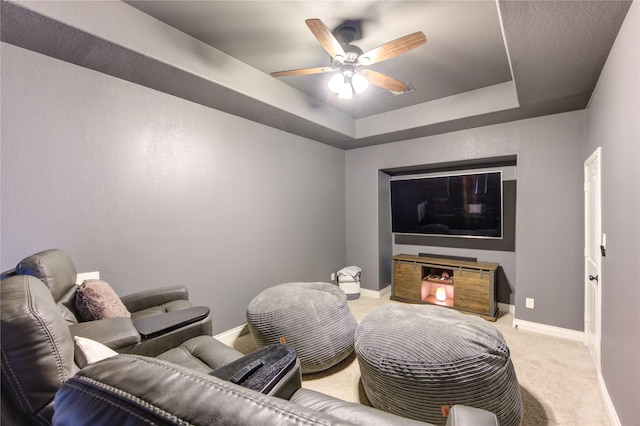 home theater featuring baseboards, ceiling fan, a tray ceiling, and light colored carpet