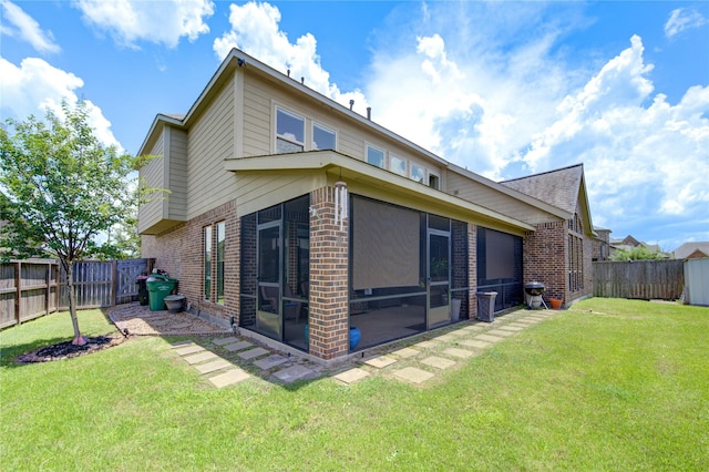 back of house with brick siding, a fenced backyard, a lawn, and a sunroom