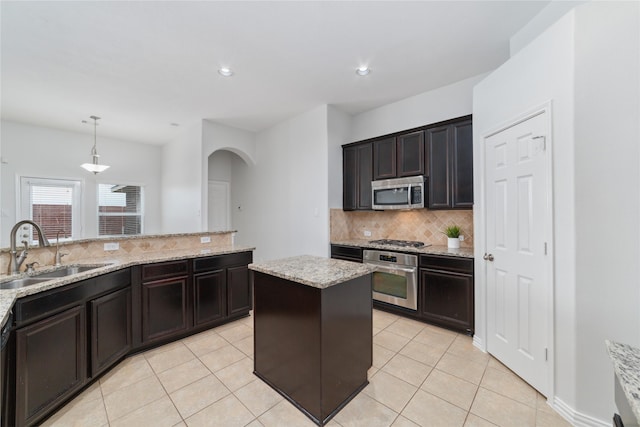 kitchen with light tile patterned flooring, appliances with stainless steel finishes, a sink, arched walkways, and backsplash