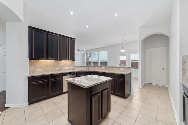 kitchen featuring a sink, a peninsula, light tile patterned floors, tasteful backsplash, and stainless steel dishwasher
