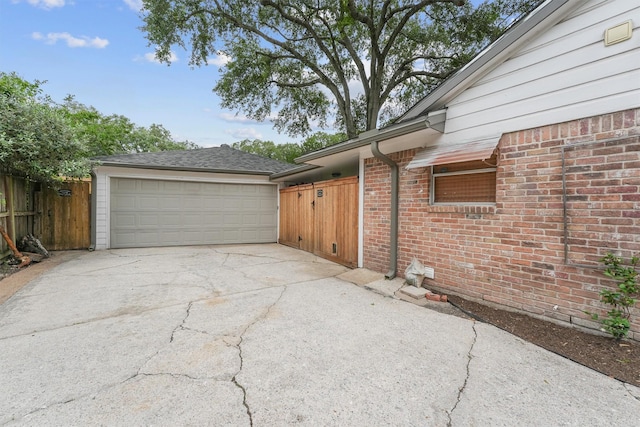 view of property exterior featuring concrete driveway, brick siding, fence, and a garage