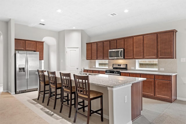 kitchen with decorative backsplash, appliances with stainless steel finishes, light stone countertops, a center island with sink, and recessed lighting