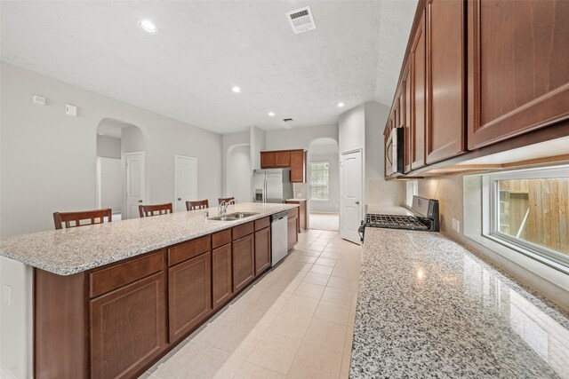 kitchen featuring arched walkways, stainless steel appliances, a large island with sink, and visible vents