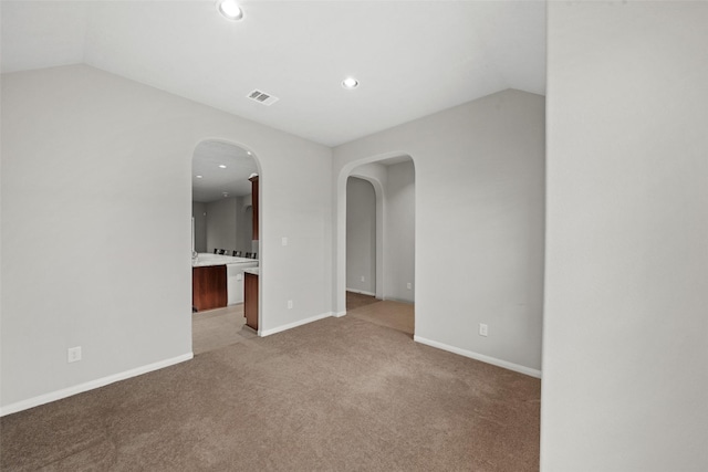 spare room featuring arched walkways, vaulted ceiling, light carpet, and visible vents