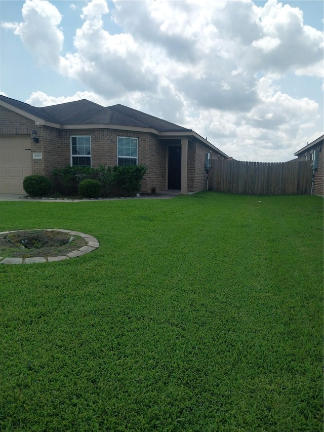 exterior space featuring brick siding, an attached garage, fence, and a yard