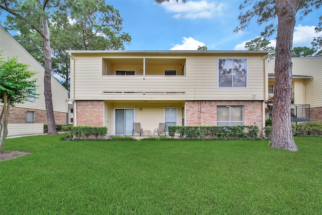 rear view of property with a lawn, brick siding, and a balcony