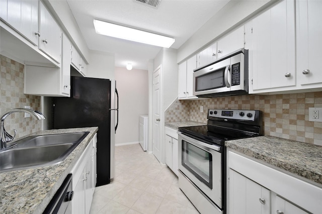 kitchen featuring appliances with stainless steel finishes, a sink, white cabinetry, decorative backsplash, and light tile patterned floors